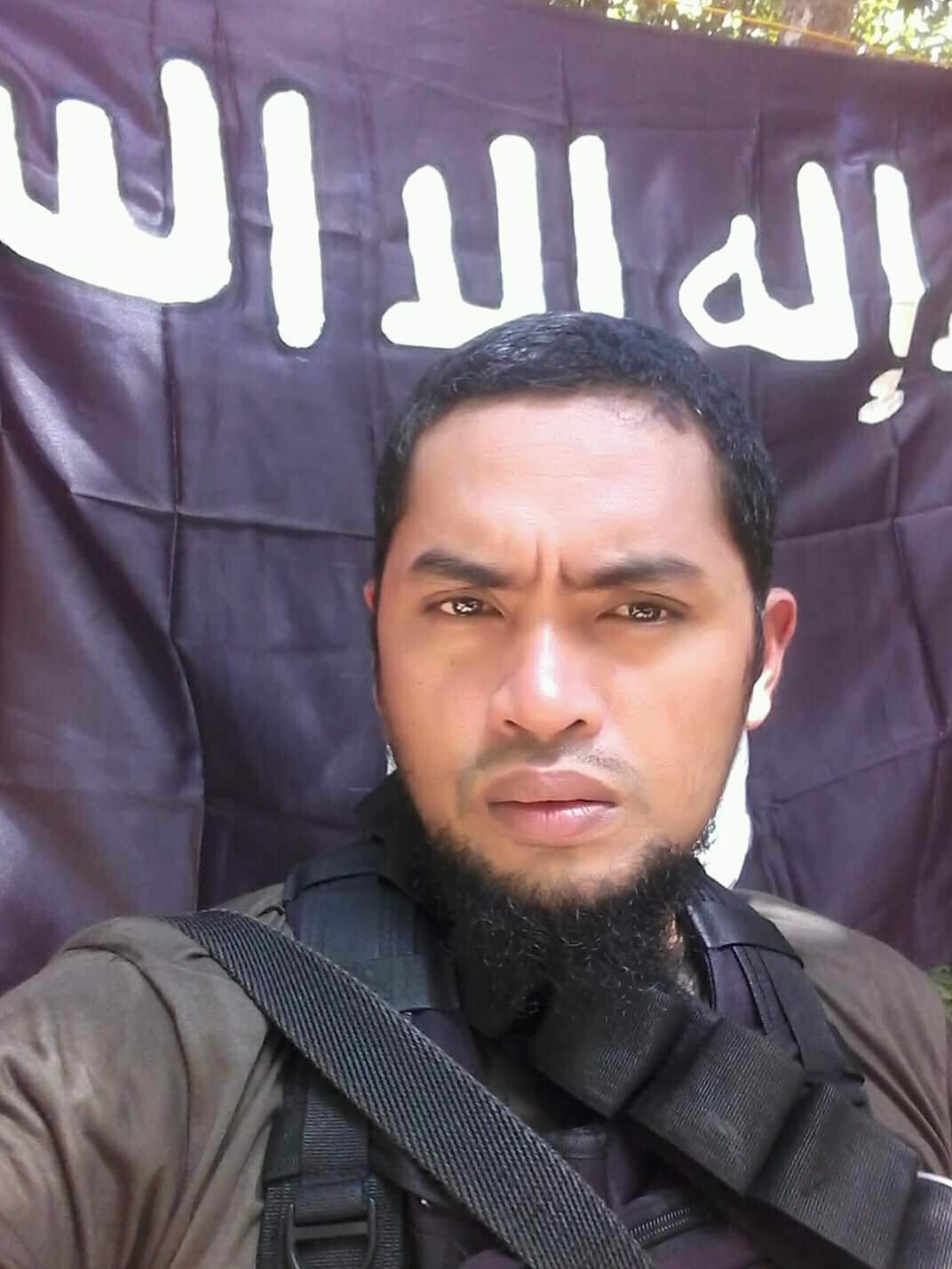 Facebook photo of Behn Tatuh, with ISIS flag behind him.