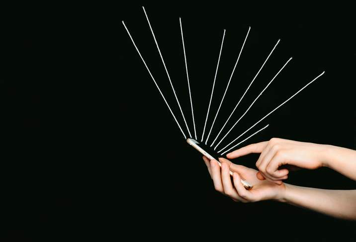 Hand holding a mobile phone, white yarn beams radiating from the phone.