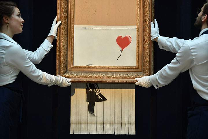 Sotheby’s employees pose with the newly completed work by artist Banksy entitled “Love is in the Bin”, a work that was created when the painting “Girl with Balloon” was passed through a shredder in a surprise intervention by the artist, at Sotheby’s auction house in London on October 12, 2018.