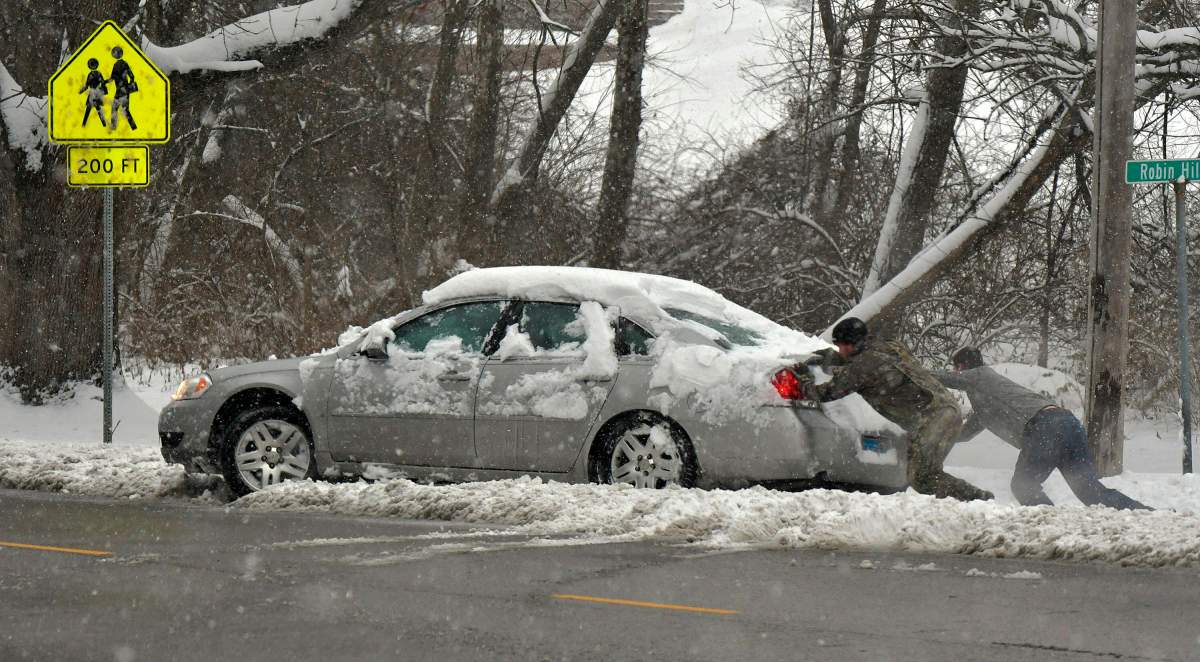 Michael Fuehne, left, and David Fellner Jr., both of Belleville, strain as they push the car of Billy Brownlee out of a pile of snow after Brownlee went sideways while making a turn in Belleville, Ill., on Saturday, Jan. 12, 2019.
