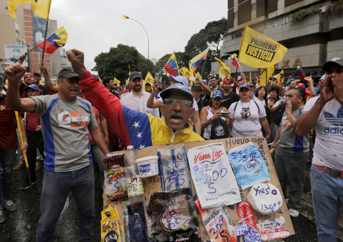 An opposition member holds a poster board with the prices of basic food during a protest against Venezuela’s President Nicolas Maduro in Caracas, Venezuela, Wednesday, Jan. 23, 2019.