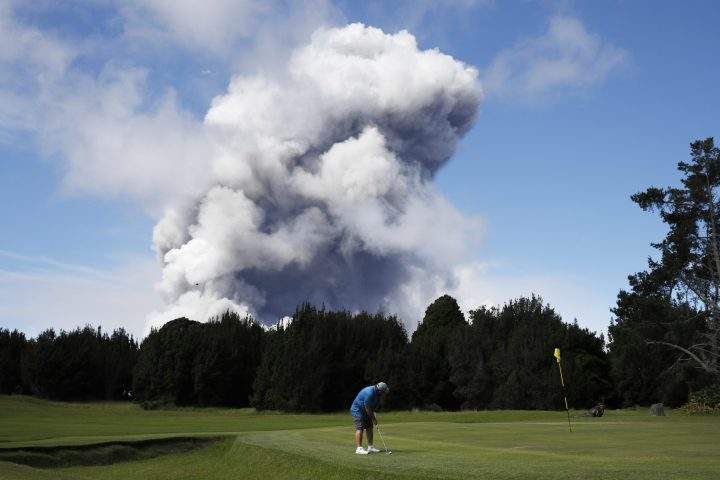 In this Monday, May 21, 2018 file photo,m Doug Ralston plays golf in Volcano, Hawaii, as a huge ash plume rises from the summit of Kiluaea volcano.