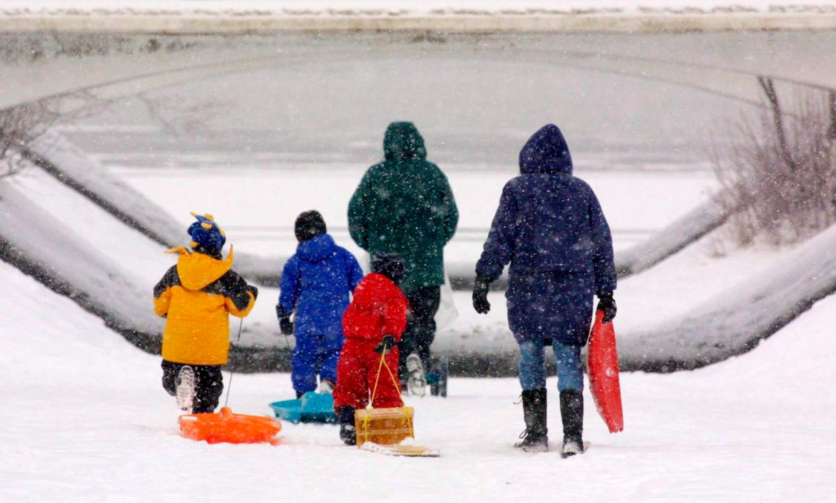 A family makes their way through the freshly fallen snow to go tobogganing.