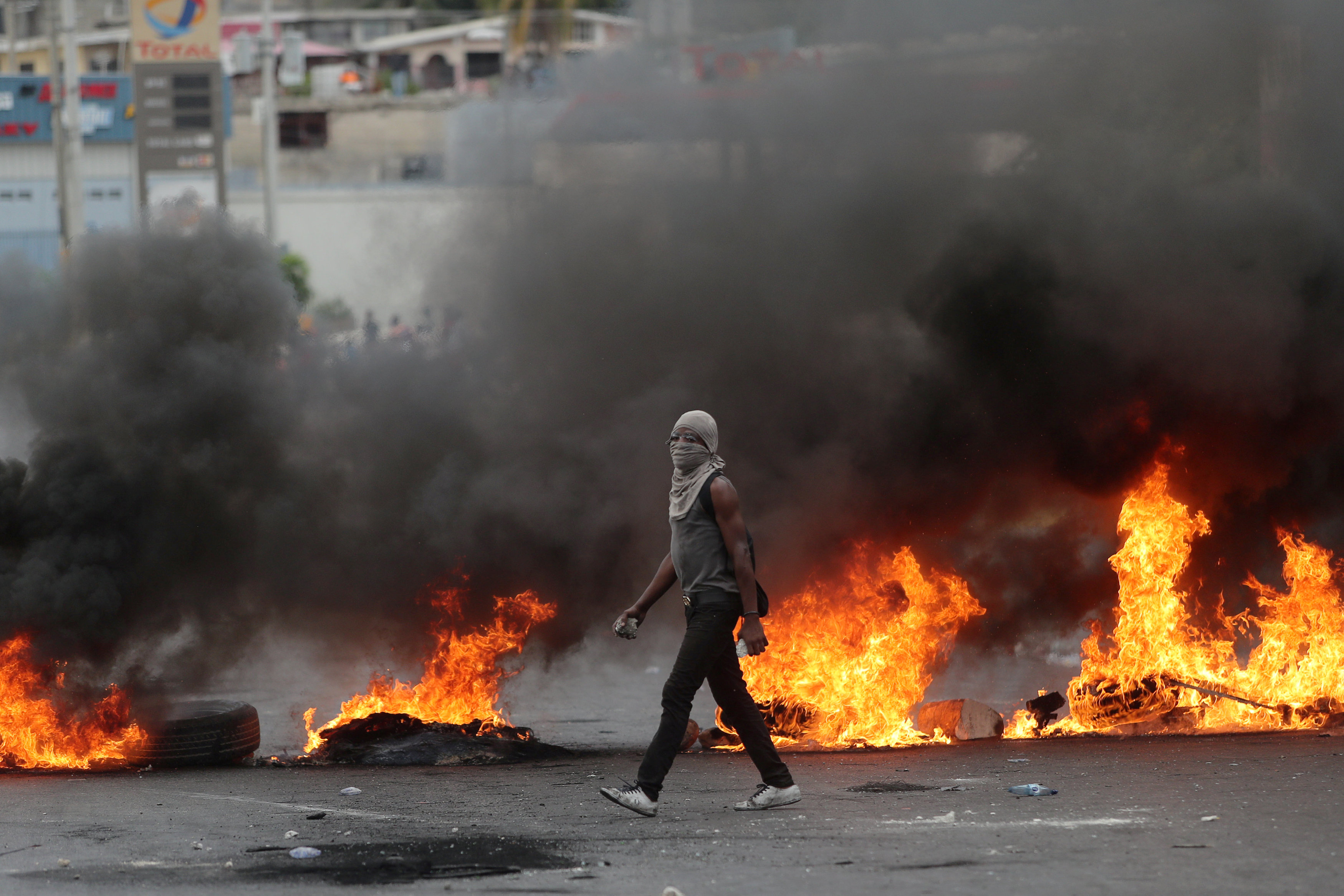 FILE – A demonstrator walks past a burning barricade during anti-government protests in Port-au-Prince, Haiti, Feb. 15, 2019.