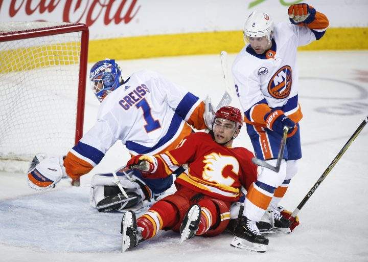 New York Islanders’ Nick Leddy, right, checks Calgary Flames’ Garnet Hathaway, centre, into goalie Thomas Greiss, of Germany, during first period NHL hockey action in Calgary, Wednesday, Feb. 20, 2019.