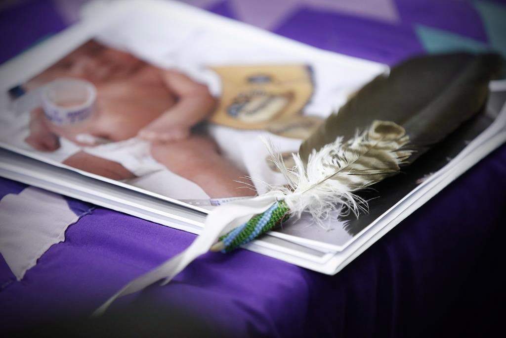 An eagle feather and a baby hospital ID bracelet sit on a photo of a newborn baby during a press conference.