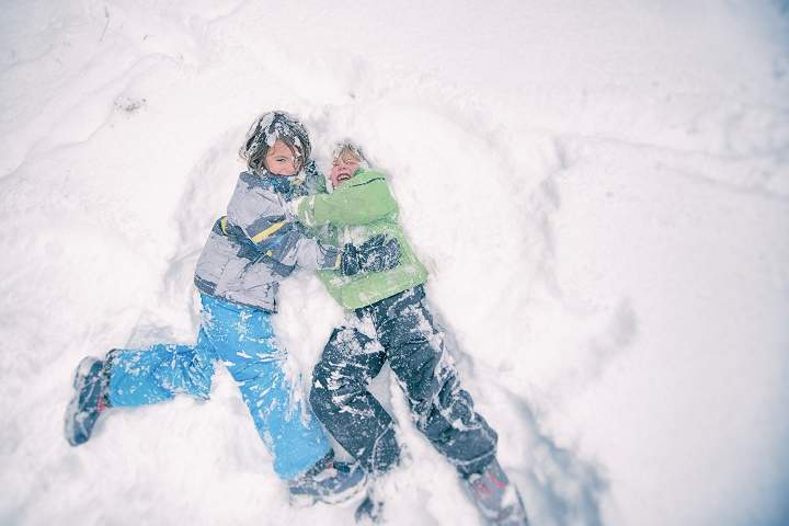 Two children wrestle playfully in the powdery snow during a storm.