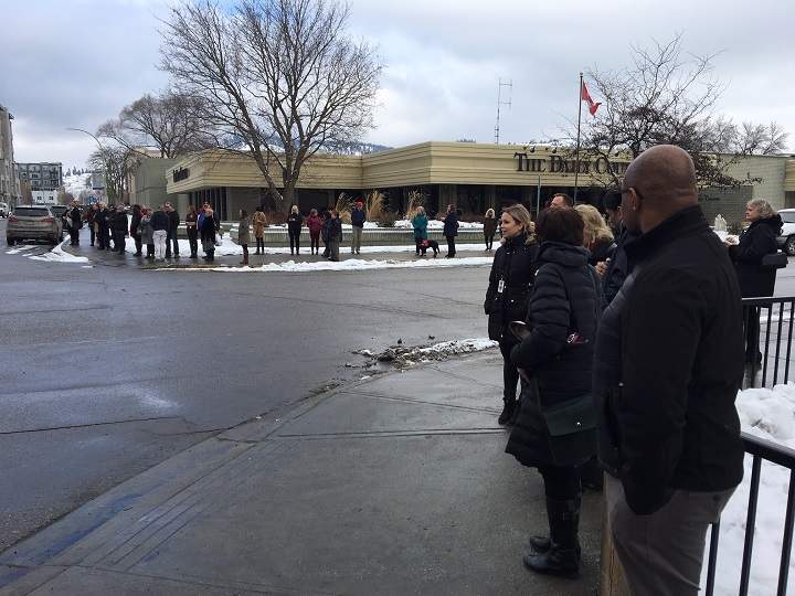 People stand on opposite corners from the Interior Health building at Doyle Avenue and St. Paul Street.