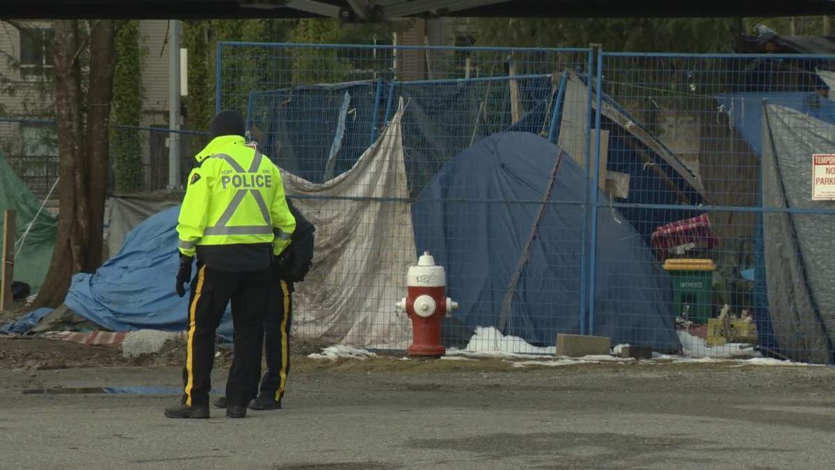 Police stand outside the Maple Ridge homeless camp known as Anita Place. A new modular housing project in the city is slated to provide shelter for residents of the camp.