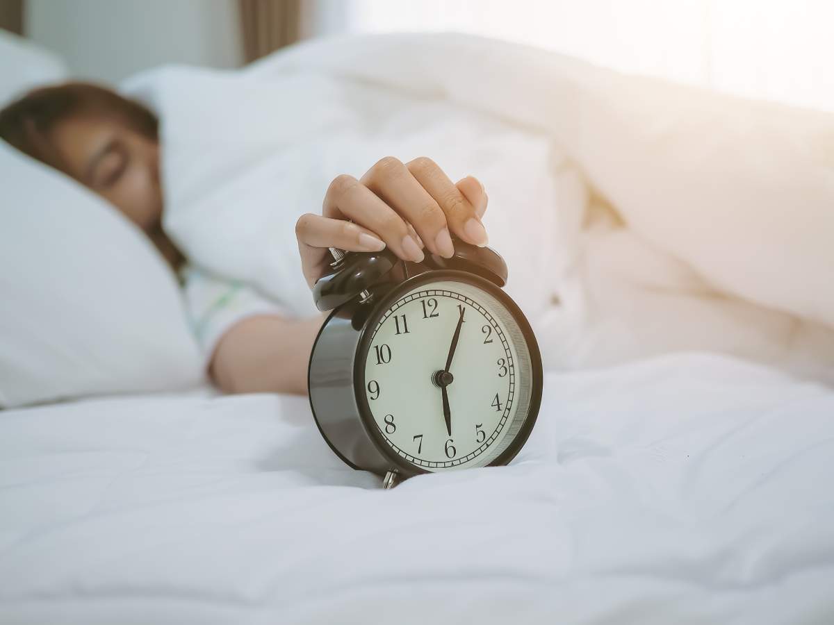 Woman snoozing Alarm Clock While Sleeping On Bed At Home.