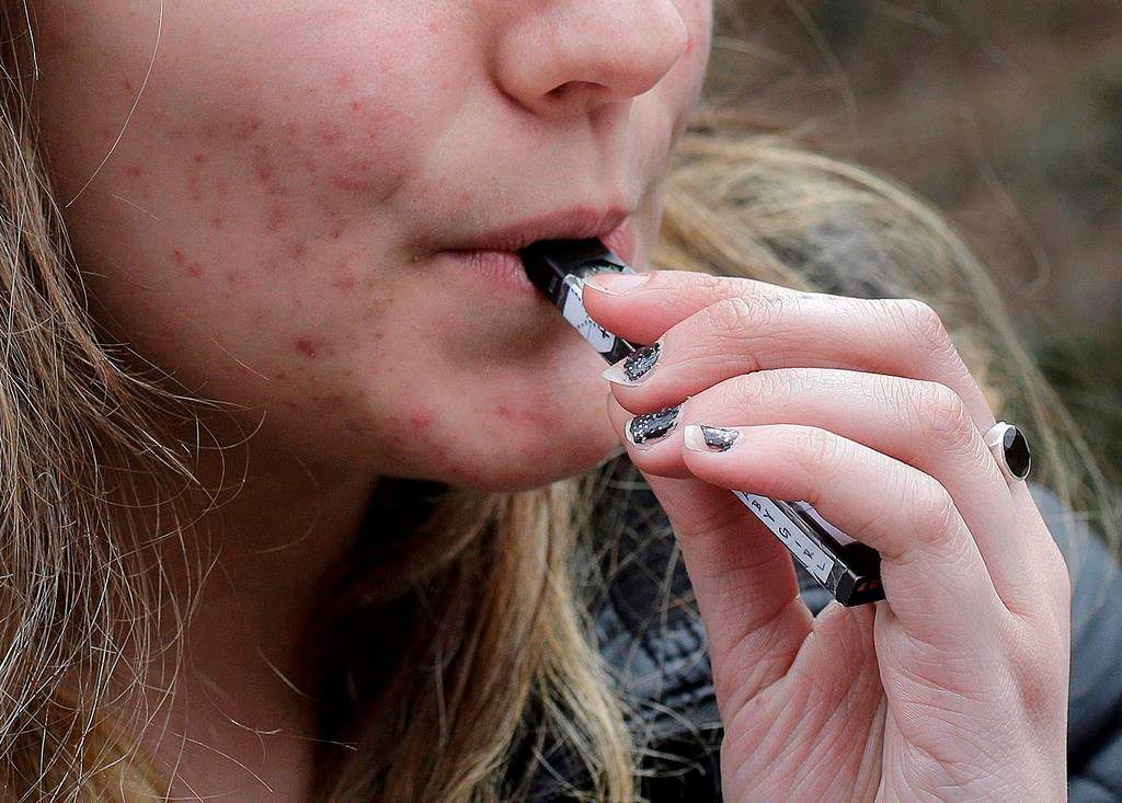 In this April 11, 2018, file photo, a high school student uses a vaping device near a school campus in Cambridge, Mass.  