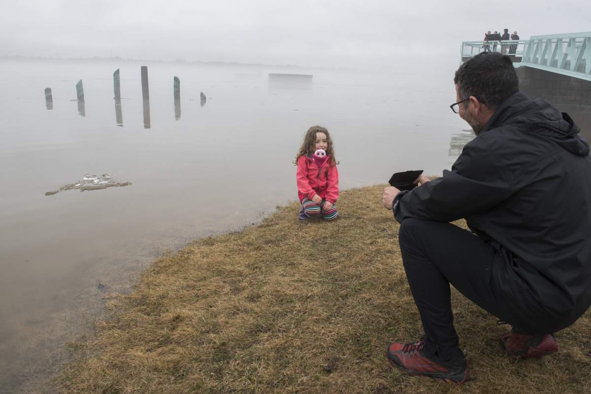Stephane Gauvreau takes a photo of his daughter Katherine, 5, next to the high water markers for the St. John River in Fredericton on Sunday, April 21, 2019.