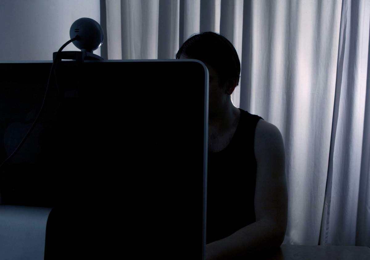 An anonymous man uses a computer equipped with a webcam.