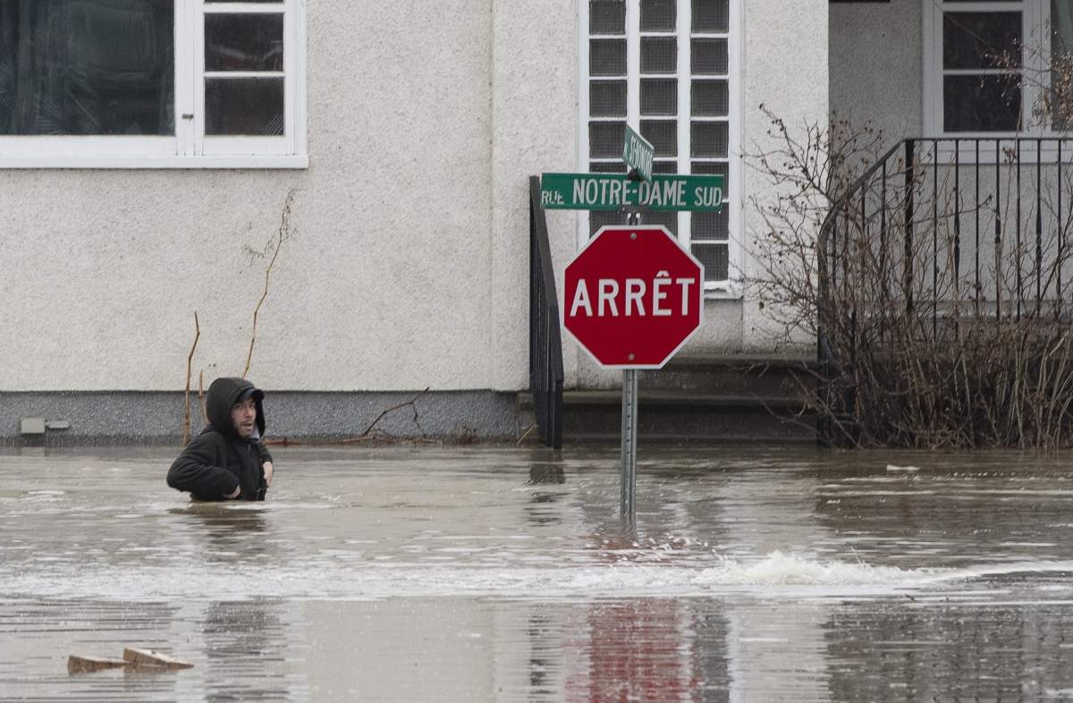 A man hops in the water of a flooded street to get to a house on Saturday, April 20, 2019, in Ste-Marie Que.