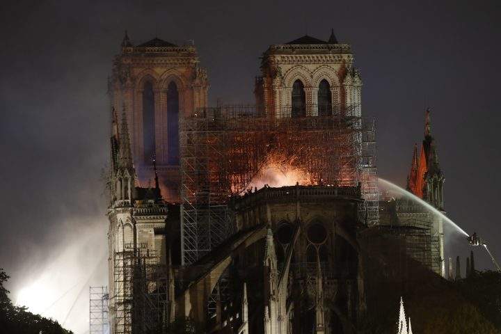 People watch Notre Dame cathedral burning in Paris, Monday, April 15, 2019. Flying buttresses can be seen connected to the structure at the bottom of the photo.