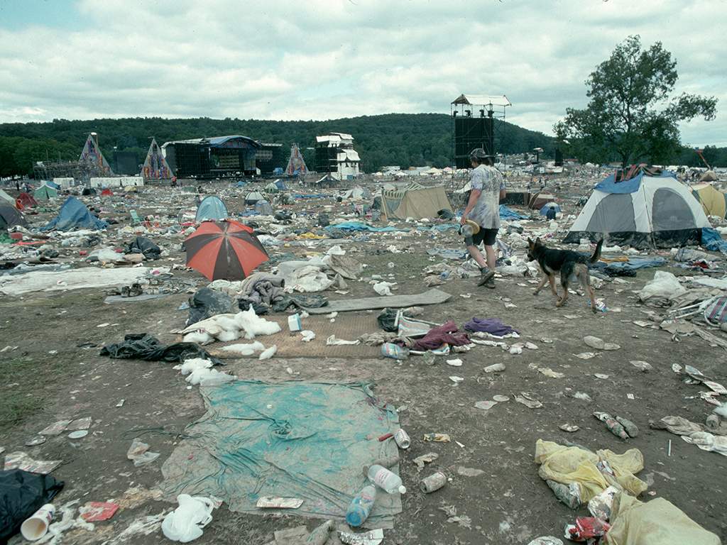 A man and his dog walk through the trash and debris left behind by festivalgoers on the concert grounds after the end of Woodstock '94, a three-day rock music festival in Saugerties, New York.  