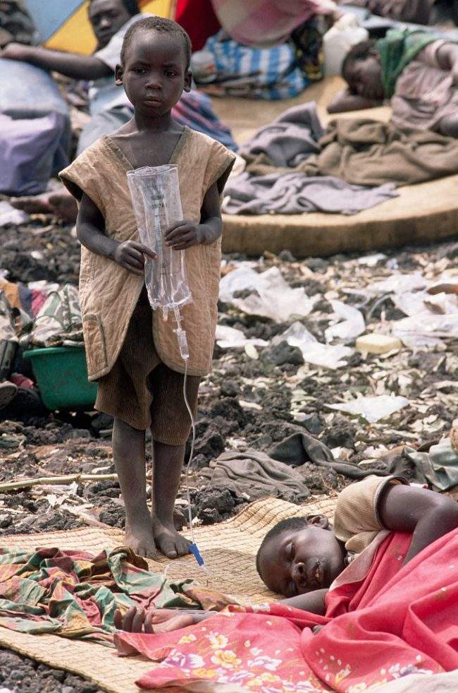 A young Rwandan Hutu refugee holds an IV bag for his mother who lies ill with cholera in a refugee camp.