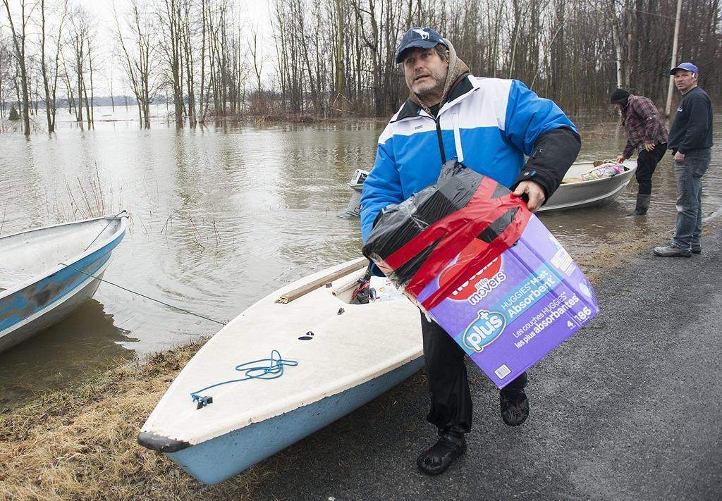 A man carries a box of personal items from a boat in the town of Rigaud, Que, west of Montreal, Friday, April 26, 2019.The town issued a mandatory evacuation order earlier Friday. THE CANADIAN PRESS/Graham Hughes