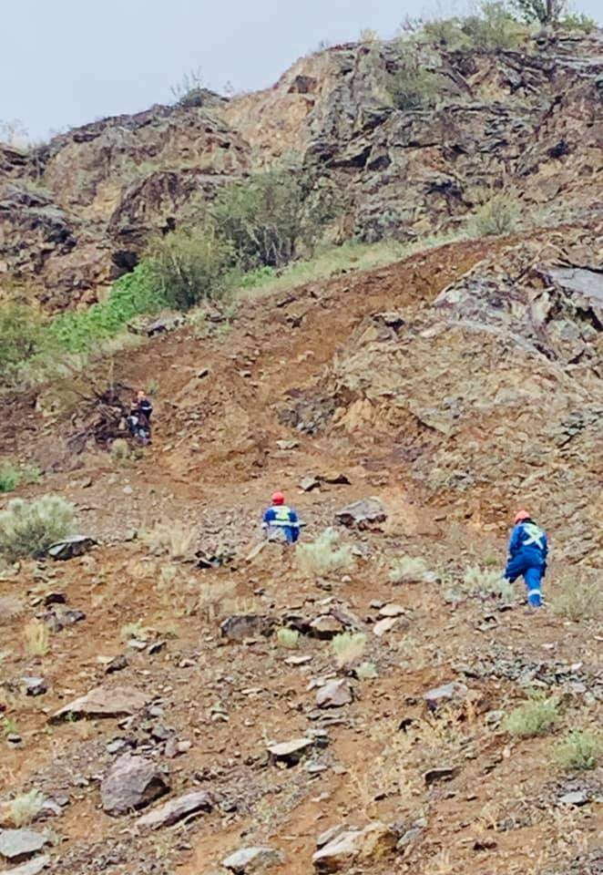 Two Osoyoos firefighters, pictured in blue uniforms, attempt to reach a stranded and terrified hiker clinging to a tree, pictured top left.