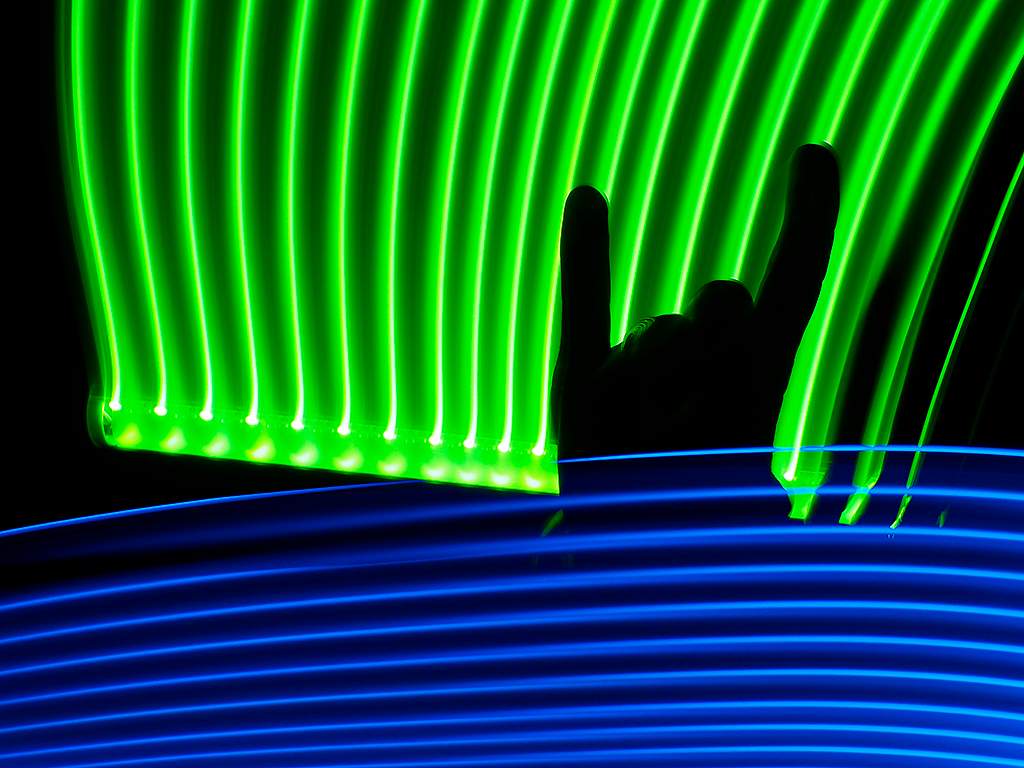 A person makes the "rock on!" sign with a neon light backdrop.