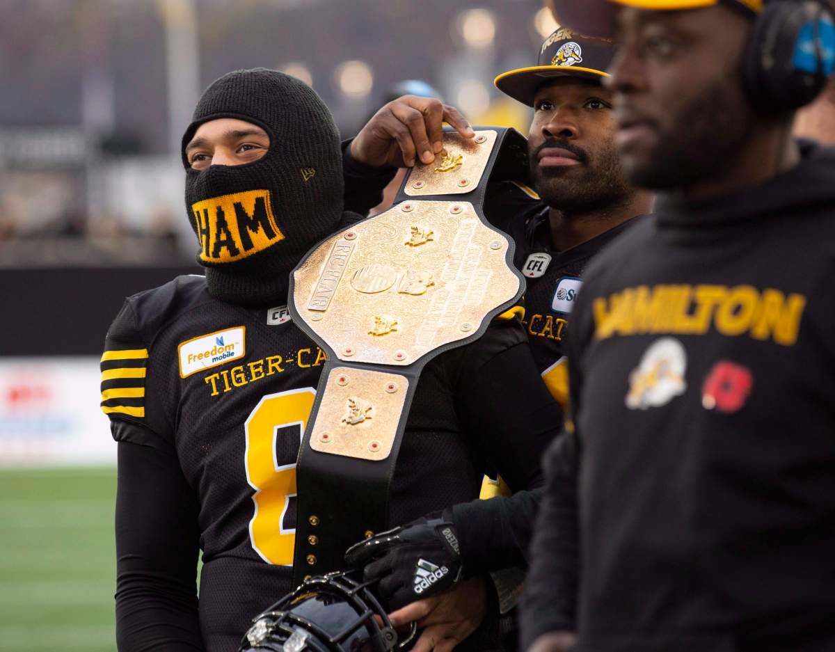 Hamilton Tiger-Cats linebacker Simoni Lawrence (21) puts a wrestling belt over the shoulder of quarterback Jeremiah Masoli (8) during second half CFL Football division semifinal game action against the B.C. Lions in Hamilton, Ont., on Nov. 11, 2018. 