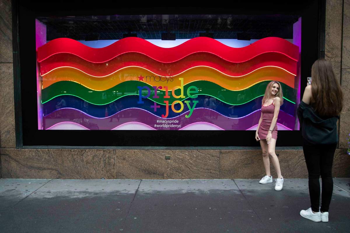In this Wednesday, June 19, 2019, photo, a visitor to Herald Square takes a photo with the Pride and Joy window display at the Macy's flagship store in New York.