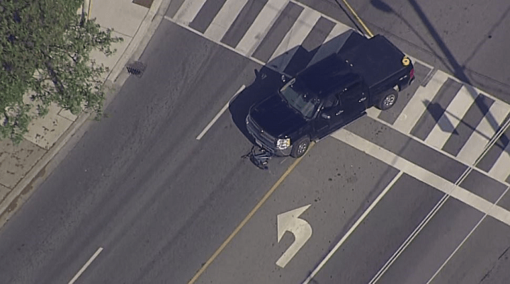 Images from the scene show a black pickup truck with what appears to be a damaged bicycle under its front end. 