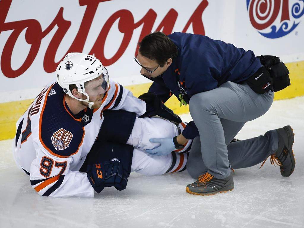 Edmonton Oilers’ Connor McDavid, left, has his knee tended too after crashing into Calgary Flames goalie Mike Smith during second period NHL hockey action in Calgary, Saturday, April 6, 2019. Connor McDavid didn’t want to answer questions about his knee. The brace hugging his left leg and an accompanying limp said enough. THE CANADIAN PRESS/Jeff McIntosh
