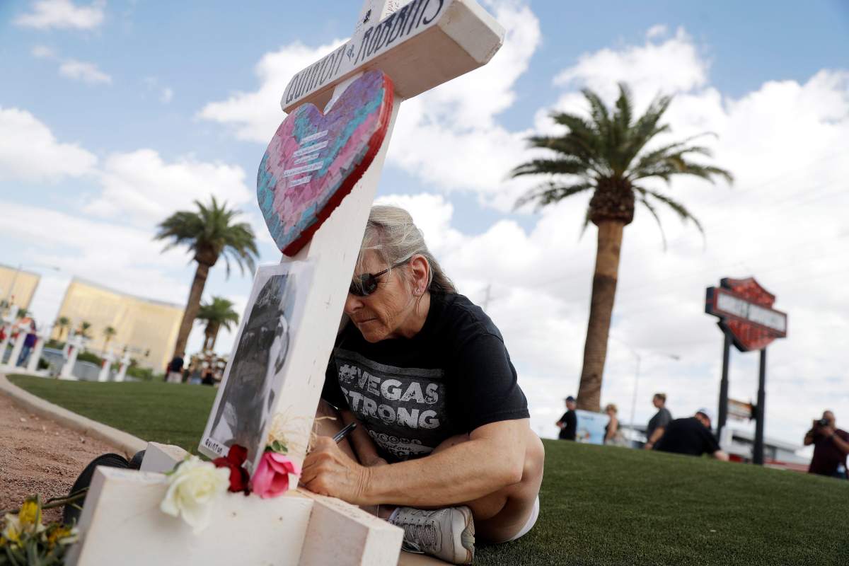 Marie Bingham writes on a memorial cross placed at the ‘Welcome to Fabulous Las Vegas’ sign for the anniversary of the Oct. 1, 2017 shooting that killed 58 and wounded hundreds in Las Vegas, Nev. USA, on Oct. 1, 2018.