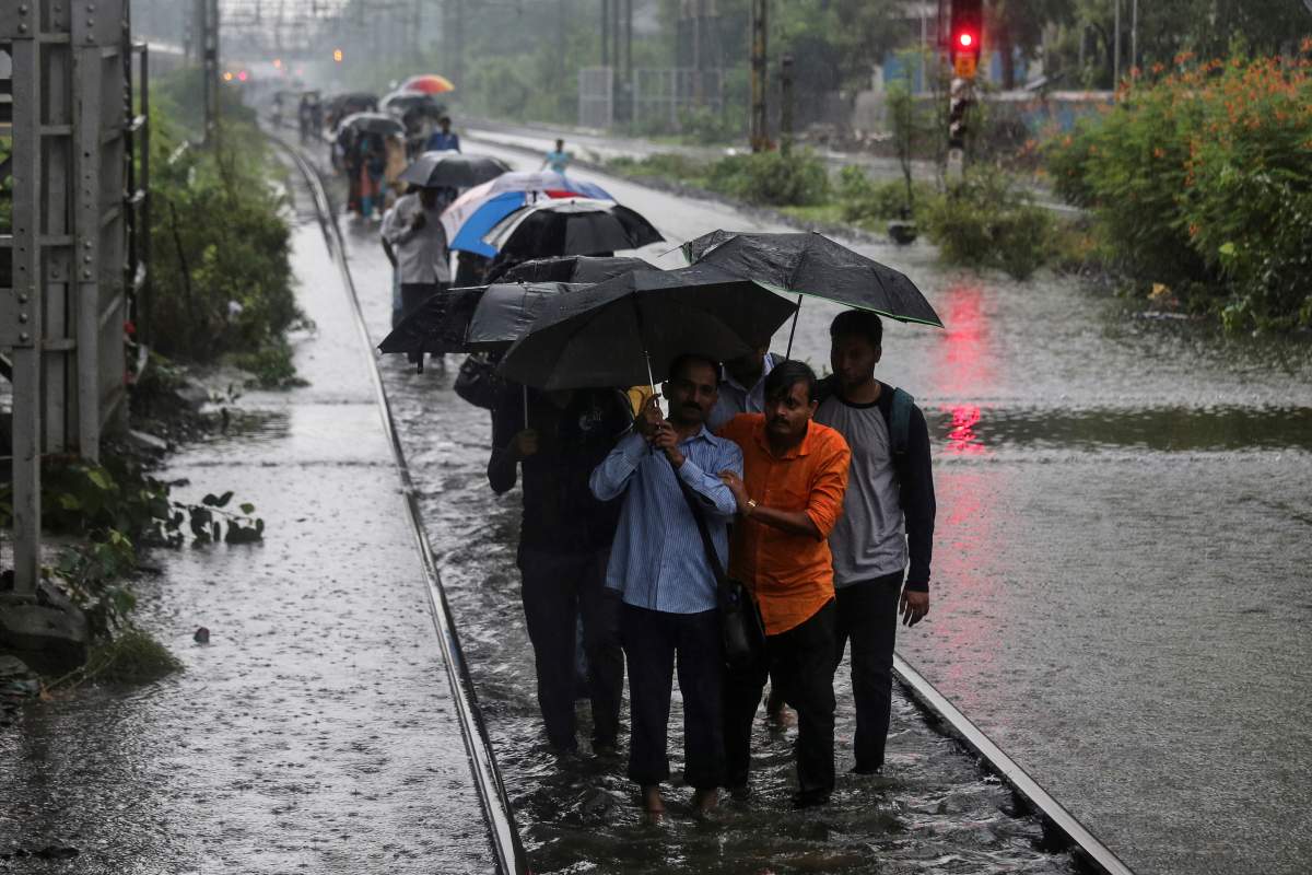 Commuters walk on waterlogged railway tracks after getting off a stalled train during heavy monsoon rains in Mumbai, India, July 2, 2019.