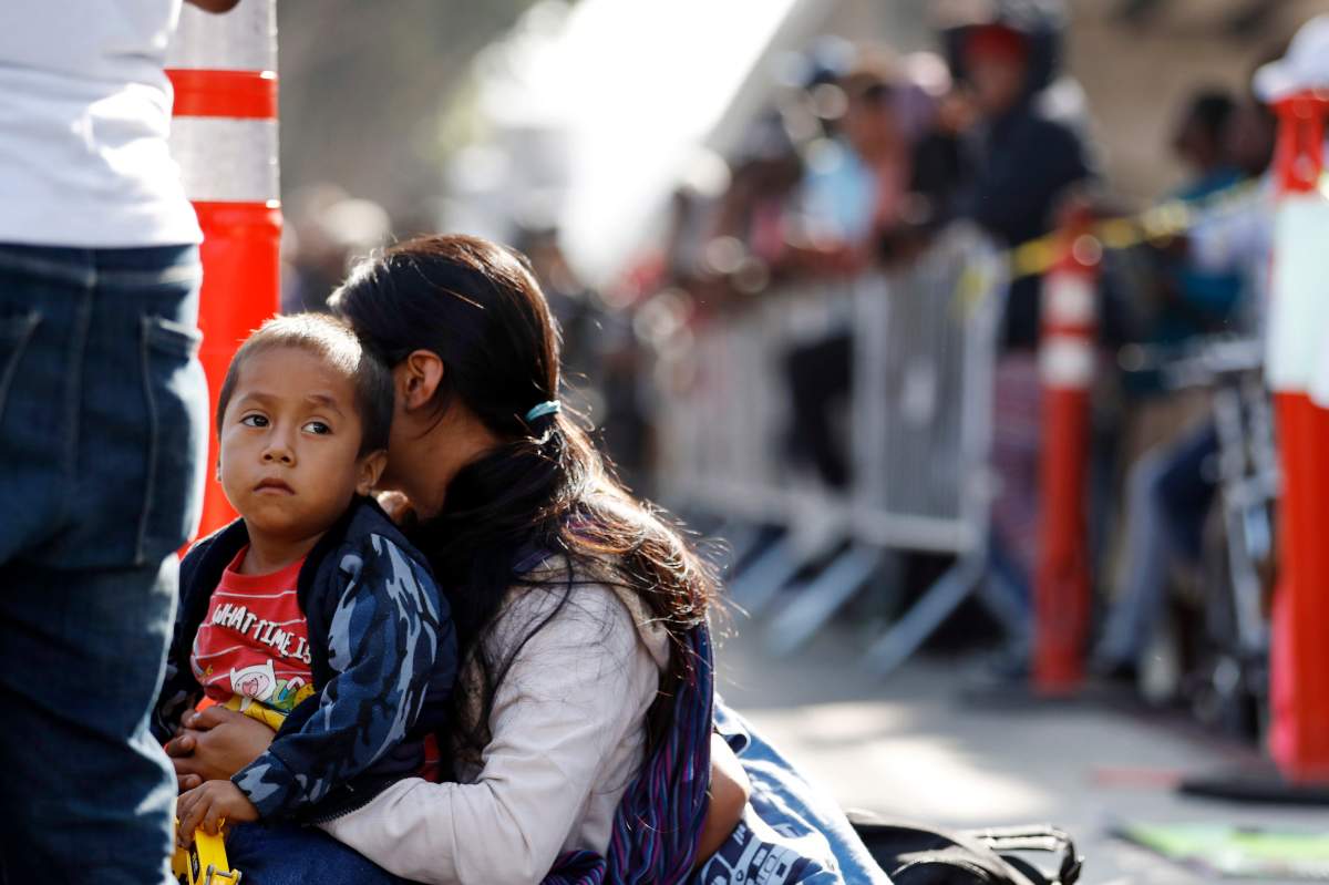 In this July 16, 2019 file photo, a woman sits with her sons as they wait to apply for asylum in the United States along the border in Tijuana, Mexico.  