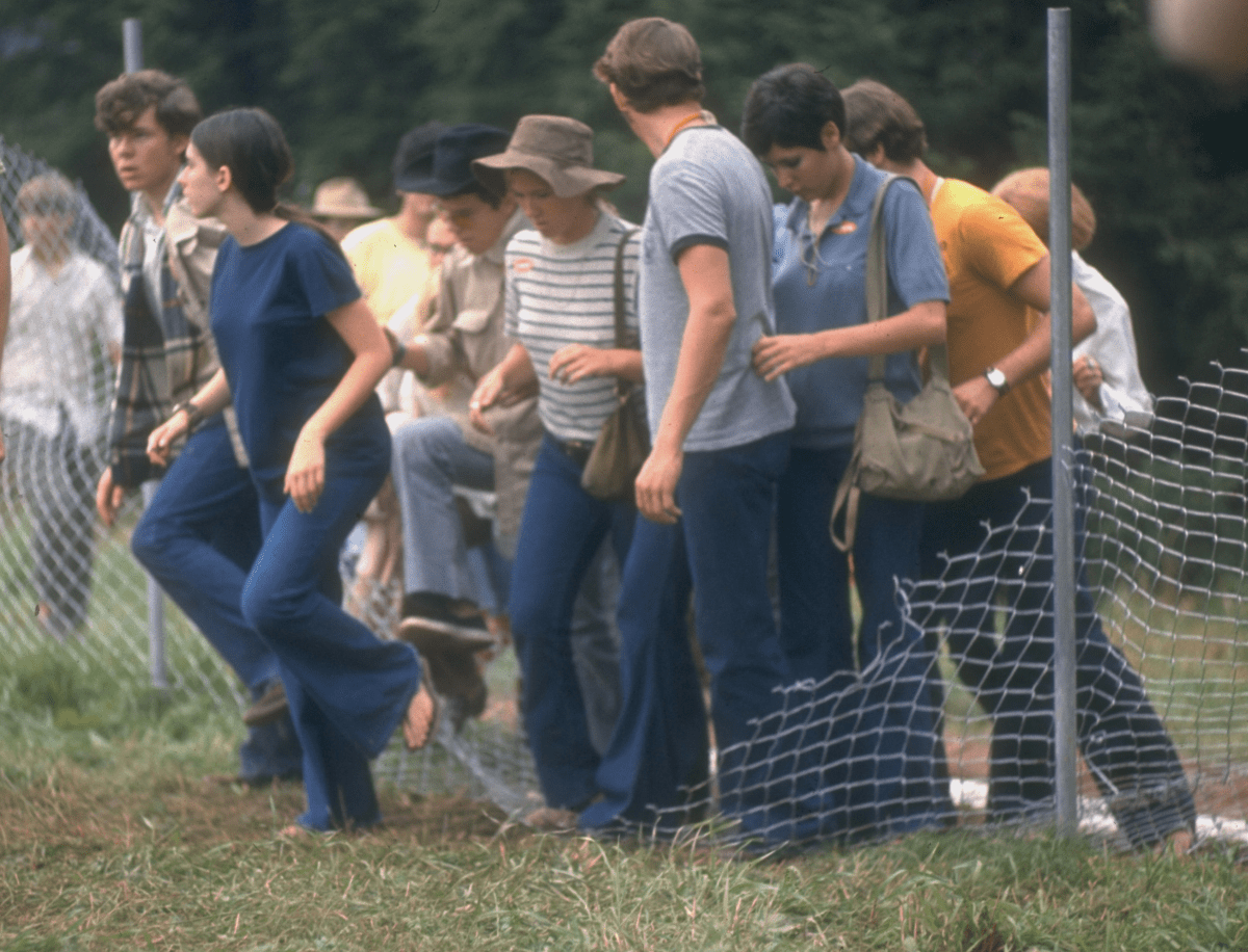 View of a group of people as they step over a torn-down fence in order to enter the grounds of the Woodstock Music & Art Festival, Bethel, N.Y., in Aug. 1969. 