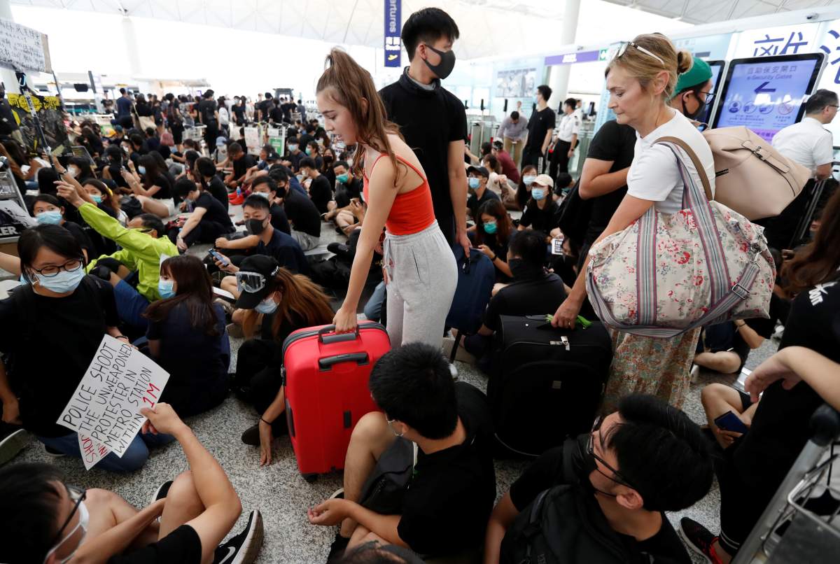 Passengers walk past anti-government protesters sitting on the floor in front of security gates during a demonstration at Hong Kong Airport, China August 13, 2019.