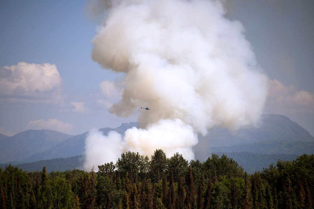 A helicopter passes by as smoke rises from a wildfire on July 3, 2019 south of Talkeetna, Alaska near the George Parks Highway.