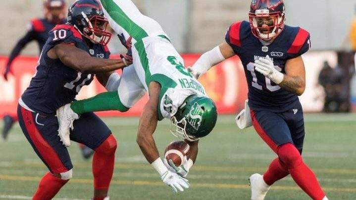 Saskatchewan Roughriders' Marcus Thigpen, centre, flips over as Montreal Alouettes' Henoc Muamba, left, as Taylor Loffler looks on during first half CFL football action in Montreal, Friday, August 9, 2019. THE CANADIAN PRESS/Graham Hughes.
