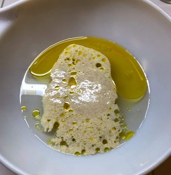 A sourdough starter is shown in a bowl with water and olive oil.