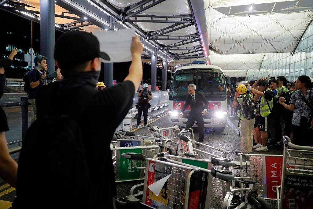 Protesters use luggage trolleys to block a police van during a demonstration at the Airport in Hong Kong, Tuesday, Aug. 13, 2019.