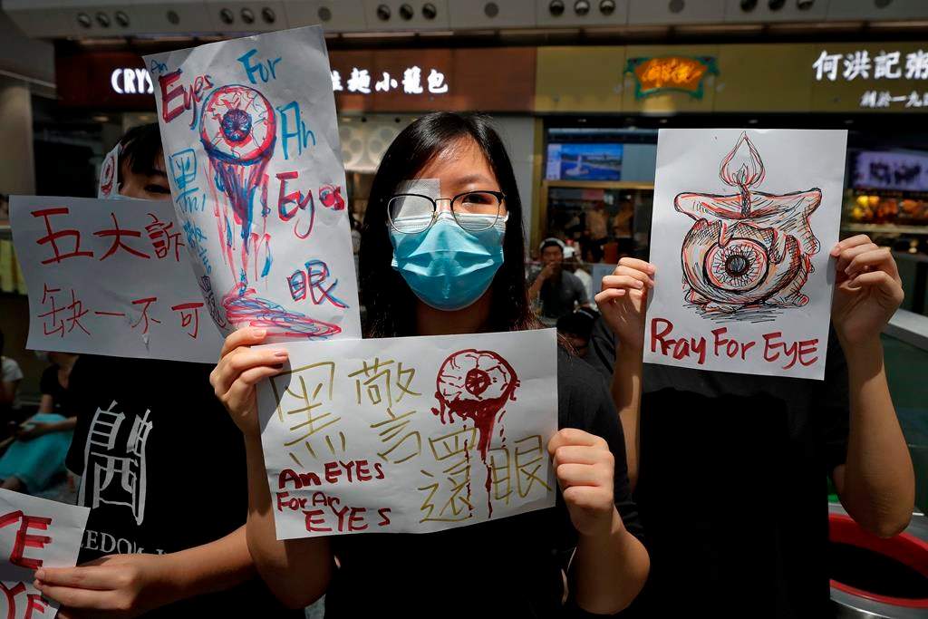 People hold signs which read ” Black Police, Return eye,” bottom center, during a protest at the arrival hall of the Hong Kong International airport in Hong Kong, Monday, Aug. 12, 2019. It is reported that police shot a woman in the eye with a projectile Sunday night during confrontations between protesters and police. (AP Photo/Vincent Thian)
