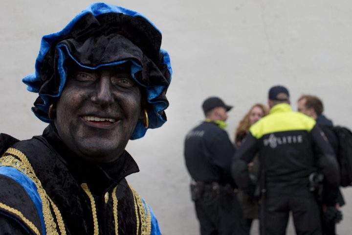 A Black Pete takes part in a far-right demonstration in a closed off area while police officers question two people, rear, during the arrival of Sinterklaas, the Dutch Saint Nicholas, in Maassluis, Netherlands, Saturday, Nov. 12, 2016.