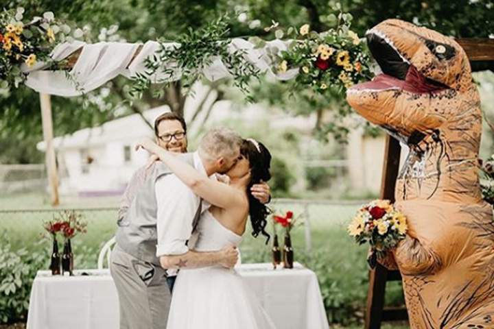 Joby and Deanna Adams share a kiss while Christina Meador stands nearby in a T. rex costume on Aug. 10, 2019, in Omaha, Neb.