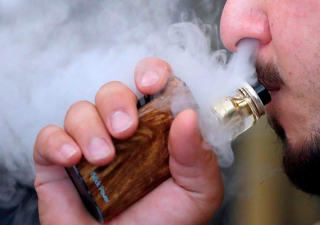 FILE - In this Friday, Aug. 17, 2018 file photo, a man breathes vapes from an e-cigarette at a vape shop in London.
