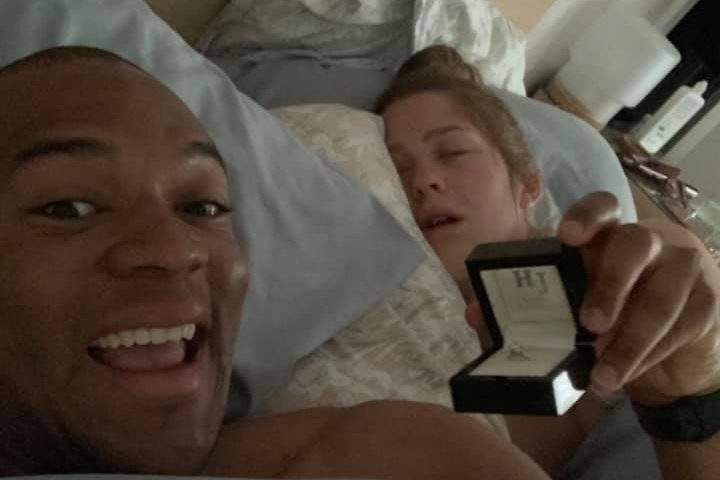 Edi Okoro, left, holds up an engagement ring while his girlfriend Cally Read sleeps next to him.