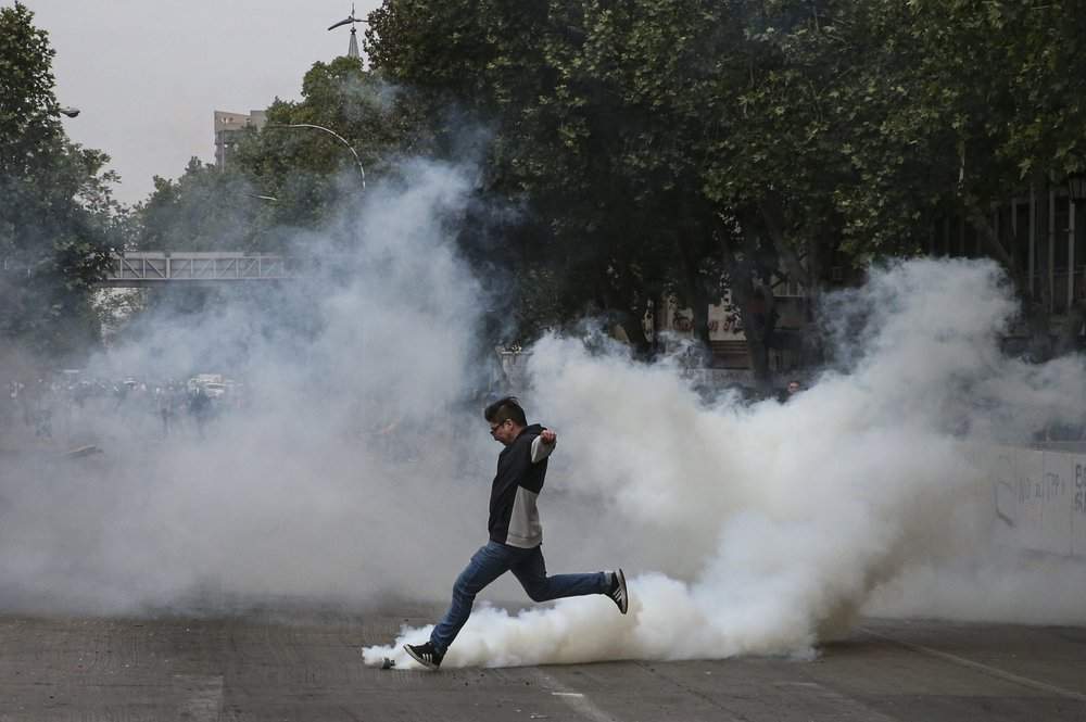 A protester kicks a tear gas canister launched by police during a protest in Santiago, Chile, Saturday, Oct. 19, 2019.