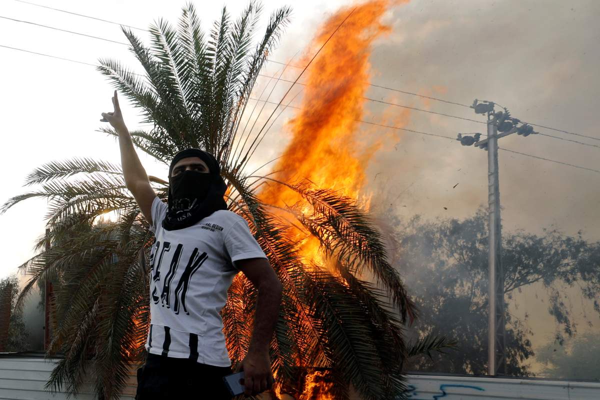 A demonstrator gestures next to a burning tree during a protest over unemployment, corruption and poor public services, in Baghdad, Iraq, on Oct. 2, 2019. REUTERS/Khalid al-Mousily
