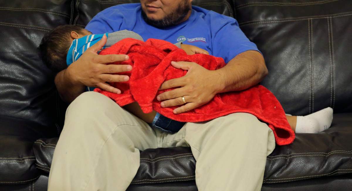 A migrant toddler is cradled by a Comprehensive Health Services, Inc. caregiver at a "tender-age" facility for babies, children and teens, in Texas' Rio Grande Valley, Thursday, Aug. 29, 2019, in San Benito, Texas. 