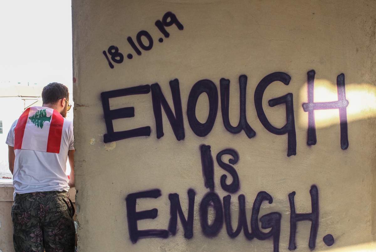 A man stands next to graffiti that spells out '18.10.2019 Enough is Enough' during a protest in downtown Beirut, Lebanon, 19 October 2019. 