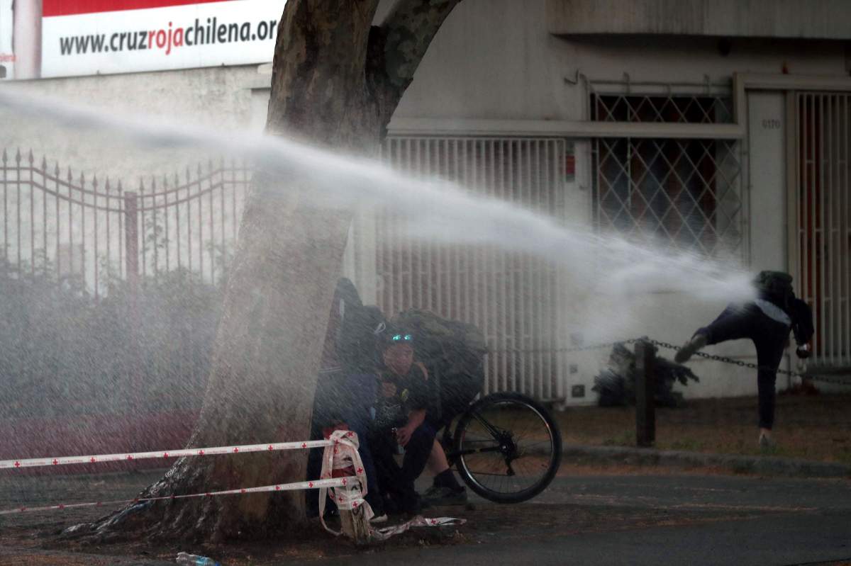 Protesters take cover from a jet of water projected from a police water cannon during anti-government protests in Santiago, Chile, 26 October 2019.