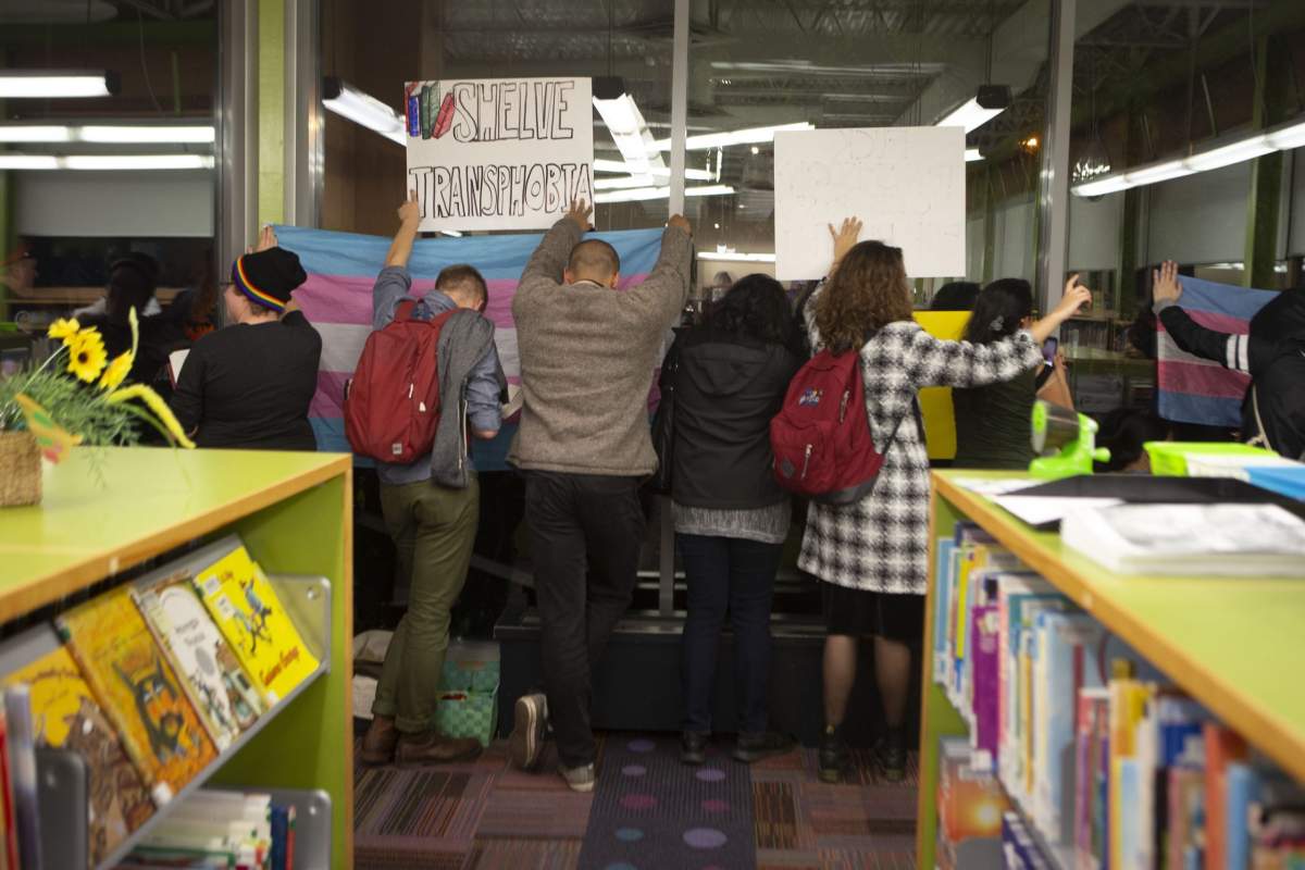Pro-transgender rights activists hold up signs on the window of a Toronto Library after writer Meghan Murphy spoke at an event on Tuesday, October 29, 2019. (THE CANADIAN PRESS/Chris Young)