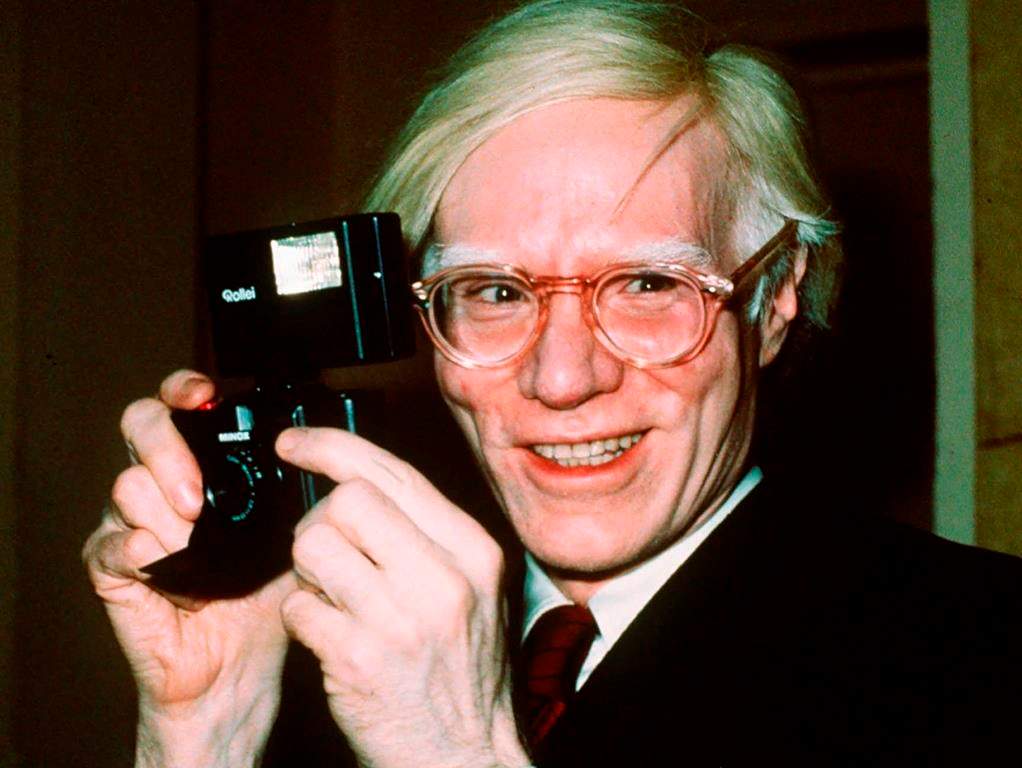 FILE - In this file photo dated 1976, showing pop artist Andy Warhol smiles in New York. Andy Warhol’s portraits of New York drag queens and trans women are going on display at London’s Tate Modern art gallery, in “a more human and personal look”, that aims to find new angles on the iconic American artist, in a show starting in March 2020.
