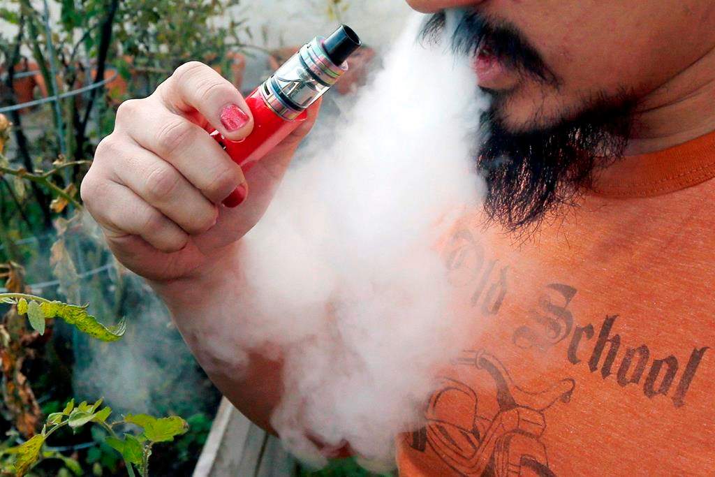FILE - In this Oct. 18, 2019 file photo, a man blows a puff of smoke as he vapes with an electronic cigarette.